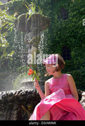 Outdoor portrait of pretty young girl in pink party dress wearing mask and holding flower. Stock Photo