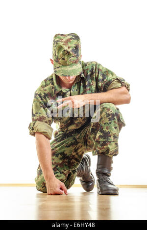 soldier with hidden face in green camouflage uniform and hat kneeling on the floor and showing the peace sign with his hand Stock Photo