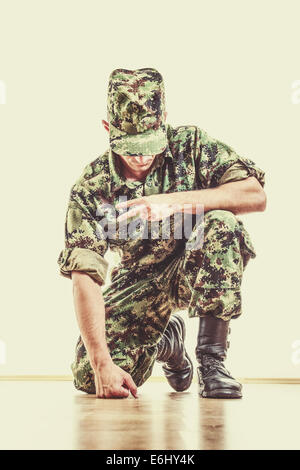 soldier with hidden face in green camouflage uniform and hat kneeling on the floor and showing the peace sign with his hand, vin Stock Photo