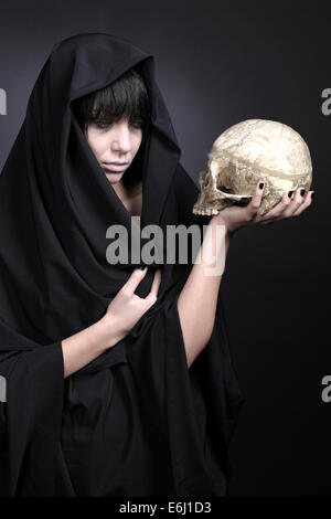 Woman with a human cranium. Covered with black cloth. Stock Photo