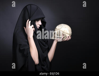 Woman with a human cranium. Covered with black cloth. Stock Photo