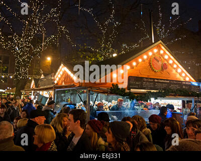 Visitors & shoppers enjoying Manchester Christmas German Markets in Albert Square , December at dusk