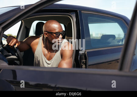 Image of handsome young man sitting in car looking away. Afro american male model sitting in car. Muscular man on road trip. Stock Photo