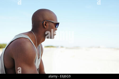 Shot of a young man wearing sunglasses outdoors. African young man sitting at the beach looking away at copy space. Stock Photo