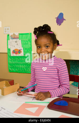 ethnic diverse girl writesl 5-6 year years old African America looking camera eye contact desk POV Myrleen Pearson Stock Photo