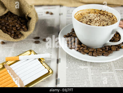 Cup of coffee, roasted beans and cigarettes arranged on a newspaper Stock Photo
