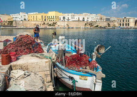 Fishermen mending  fishing nets and cleaning boats at the quay in the old town of Gallipoli, Puglia, Southern Italy. Stock Photo