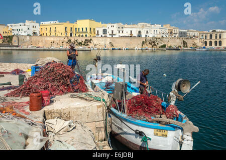 Fishermen mending  fishing nets and cleaning boats at the quay in the old town of Gallipoli, Puglia, Southern Italy. Stock Photo
