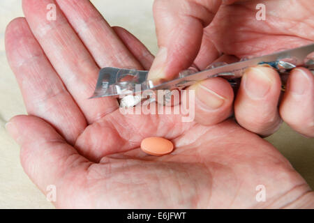 A senior woman taking pressing a Simvastatin 40 mg tablet out of a foil blister pill pack in to a hand for high cholesterol treatment. England UK Stock Photo