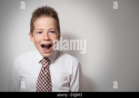 The cute smiling screaming boy teenager in a white shirt and a tie on a gray background with place for text Stock Photo