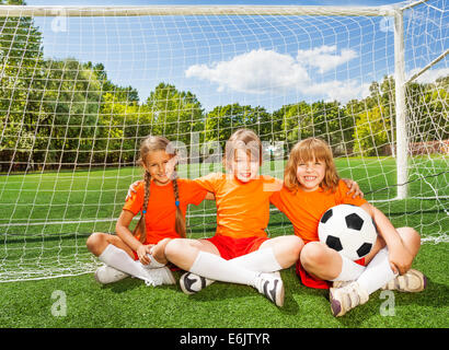 Smiling children sitting on grass with football Stock Photo