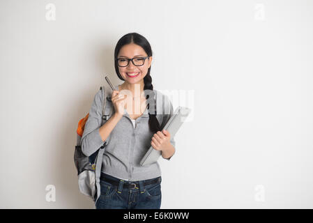 asian college girl thinking holding a pen with laptop on plain background Stock Photo