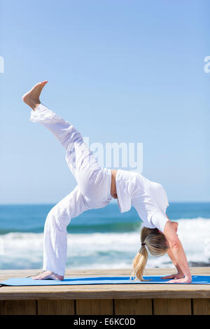 flexible mature woman practicing yoga by the beach Stock Photo