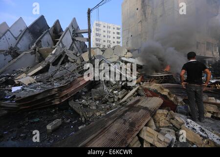 Gaza City, Gaza Strip, Palestinian Territory. 26th Aug, 2014. Fire is seen as a Palestinian man walks amidst the remains of a tower building housing offices, which witnesses said was destroyed by an Israeli air strike, in Gaza City August 26, 2014. Israeli air strikes launched before dawn on Tuesday killed two Palestinians and destroyed much of one of Gaza's tallest apartment and office buildings, setting off huge explosions and wounding 20 people. Credit:  ZUMA Press, Inc./Alamy Live News Stock Photo