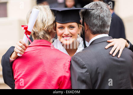 gorgeous university female graduate hugging her parents after graduation Stock Photo