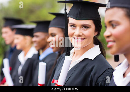 smiling female college graduate standing with friends at graduation Stock Photo