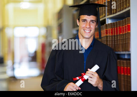 handsome male graduate wearing graduation gown in library Stock Photo