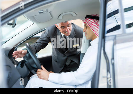 friendly senior salesman explaining car features to Arabian man Stock Photo