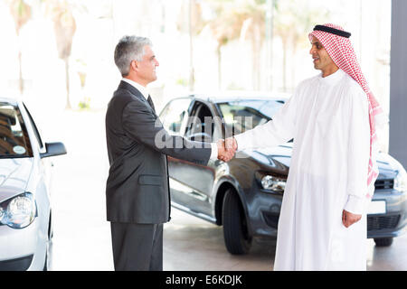 smiling middle aged car dealer handshake with Arabian man Stock Photo