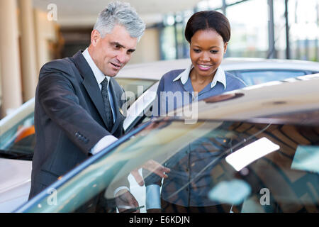 friendly mature car dealer showing new car to African customer Stock Photo