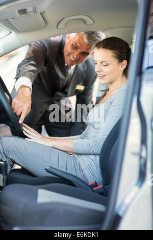 middle aged car salesman showing car features to young customer Stock Photo