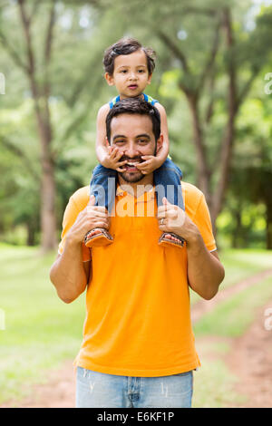 cheerful Indian father carrying son on his shoulders in the park Stock Photo