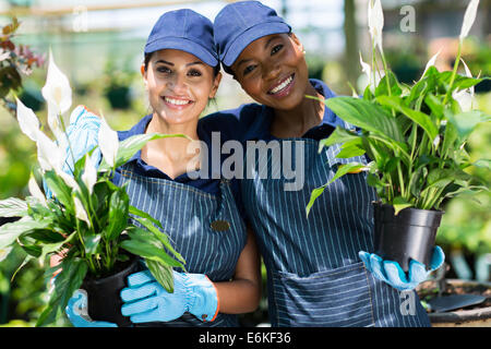 cute female nursery co-workers with pot of flowers inside greenhouse Stock Photo