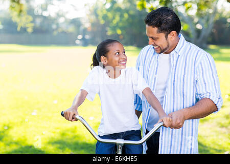loving Indian father teaching daughter to ride a bicycle at the park Stock Photo