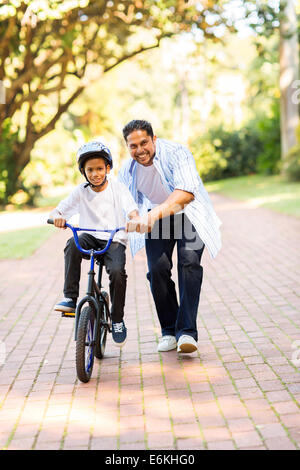 happy Indian father teaching his son to ride a bicycle at the park Stock Photo