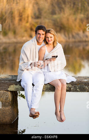 romantic couple sitting on pier and drinking wine at sunset Stock Photo