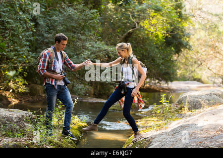 young man helping girlfriend crossing stream at mountain valley Stock Photo