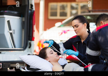 young female EMT putting oxygen mask on unconscious patient Stock Photo