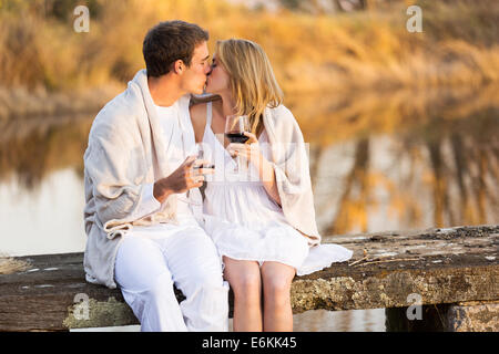 romantic couple kissing on a pier and holding glass of wine at sunset