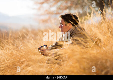 handsome man sitting in tall grass in autumn Stock Photo