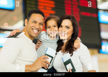 portrait of family holding passports and boarding pass in front of flight information board Stock Photo