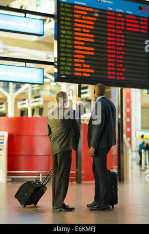 rear view of business partners checking flight information at airport Stock Photo