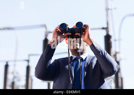 African American electrical manager using binoculars looking at substation Stock Photo