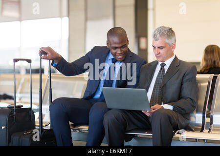 two businessmen working on laptop computer at airport Stock Photo
