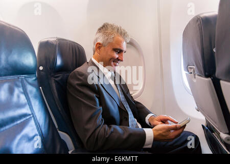happy middle aged businessman using cell phone on airplane Stock Photo