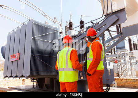 back view of electricians standing next to a transformer in electrical power plant Stock Photo