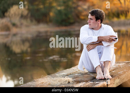 thoughtful young man drinking wine alone by a lake Stock Photo