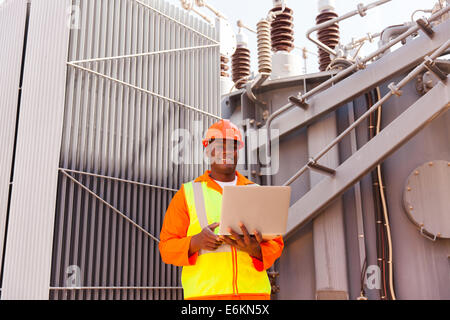 African electrician using laptop in front of transformer Stock Photo