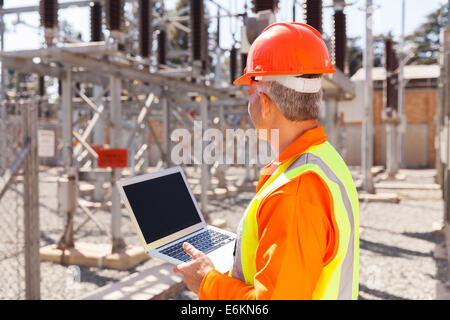 senior technician holding laptop computer in substation Stock Photo