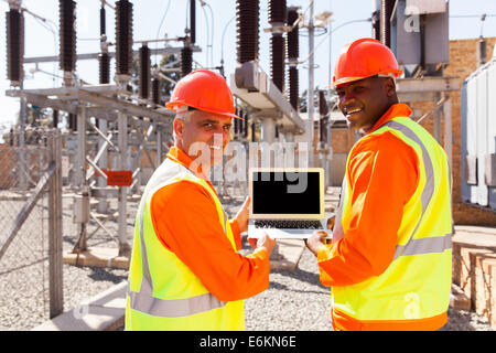 happy electrical engineers holding laptop computer in power plant Stock Photo