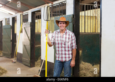 happy horse farmer holding pitch fork in stable Stock Photo