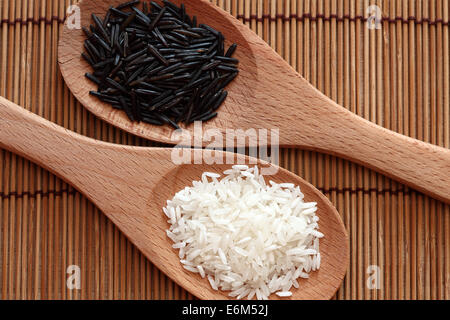 White rice and wild rice in a wooden spoons on bamboo napkin. Closeup. Stock Photo