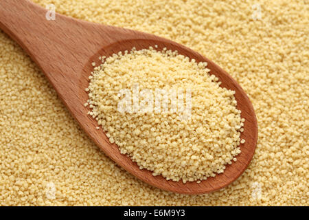 Couscous in a wooden spoon on couscous background. Stock Photo