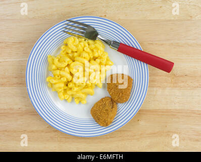 Top view of a meal of macaroni and cheese with two chicken nuggets on a blue striped plate with a red handled fork on a wood tab Stock Photo