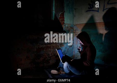 Female computer hacker sitting with a laptop in the dark, in an old building Stock Photo