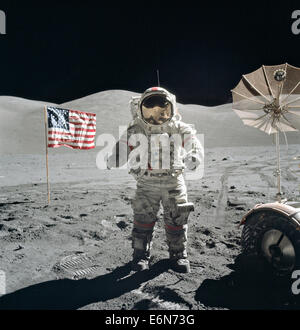 NASA astronaut Eugene Cernan, Commander, Apollo 17, flanked by an American flag and their lunar rover's umbrella-shaped high-gain antenna at the Taurus-Littrow landing site December 13, 1972. The prominent Sculptured Hills lie in the background while Schmitt's reflection can just be made out in Cernan's helmet. While astronauts Cernan and Jack Schmitt descended in the Challenger to explore the Taurus-Littrow region of the Moon, astronaut Ronald E. Evans, Command Module pilot, remained with the Command Service Module 'America' in lunar-orbit. Stock Photo